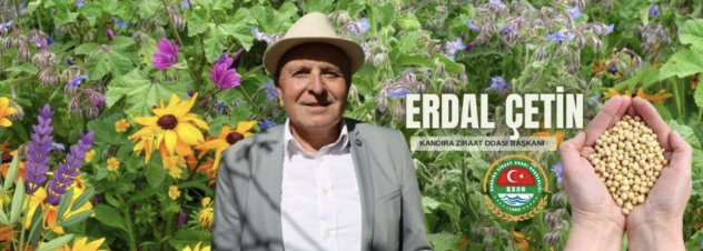 Kandıra Ziraat Odası Başkanı Erdal Çetin, arka planda renkli çiçeklerle çevrili bir bahçede, elinde tohum tutarak gülümsemektedir.