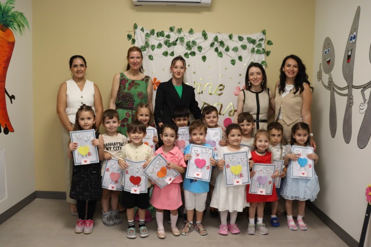 Çınar Çocuk Evleri'nde karne törenine katılan çocuklar, öğretmenleri ve İzmit Belediyesi yetkilileriyle birlikte fotoğraf çektiriyor. Çocuklar ellerinde karneleriyle gülümsüyor.