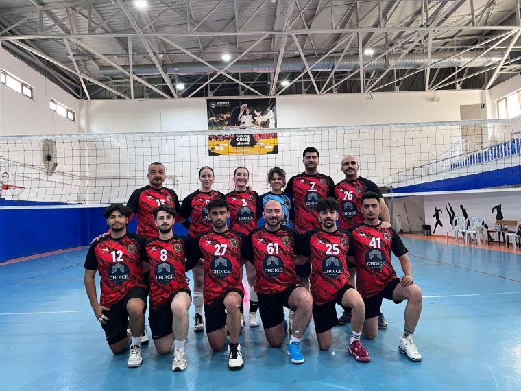 Voleybol takımı, sahada forma giymiş oyuncularla birlikte poz veriyor. Arka planda voleybol filesi ve spor salonu görülüyor.
