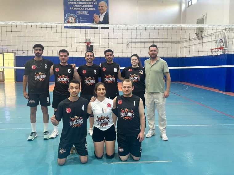 Dracaryus voleybol takımının sporcuları, turnuva öncesinde poz veriyor. Arka planda voleybol fileleri ve antrenman alanı bulunuyor.
