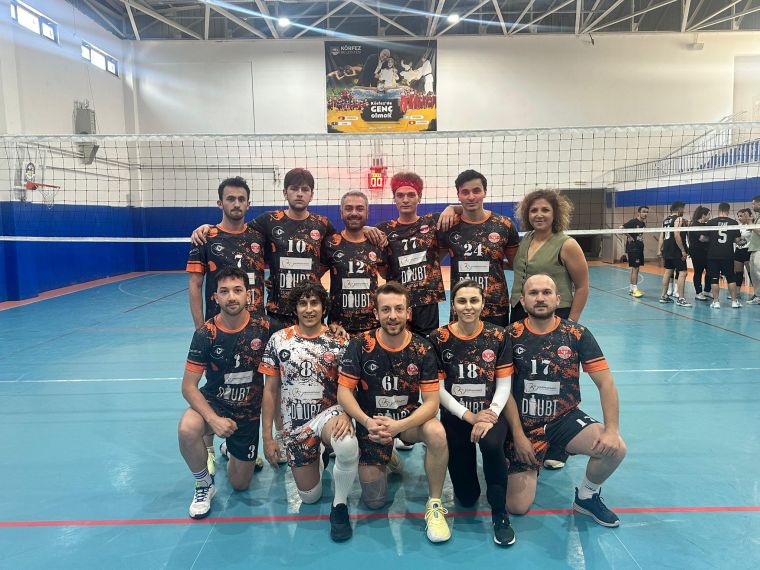 Bir voleybol takımının oyuncuları, salonda bir araya gelmiş, takım formalarıyla poz vermekte. Arkada voleybol filesi ve salonun diğer bölümünde oyuncular mevcut.