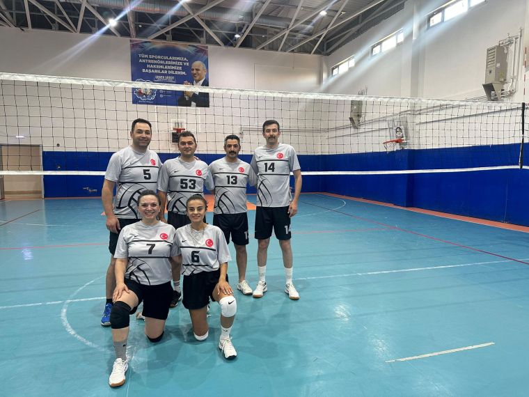 Bir voleybol takımı, salonda file önünde poz veriyor. Her oyuncu takım forması giymekte ve gülümsemekte.