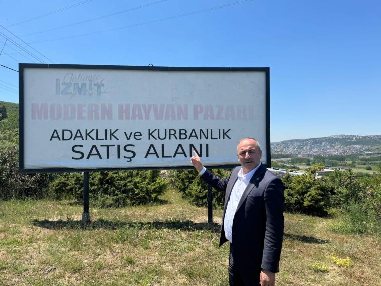 A man in a suit points at a sign indicating 'Modern Hayvan Pazarı' with the subtext 'Adaklık ve Kurbanlık Satış Alanı' in a rural setting.