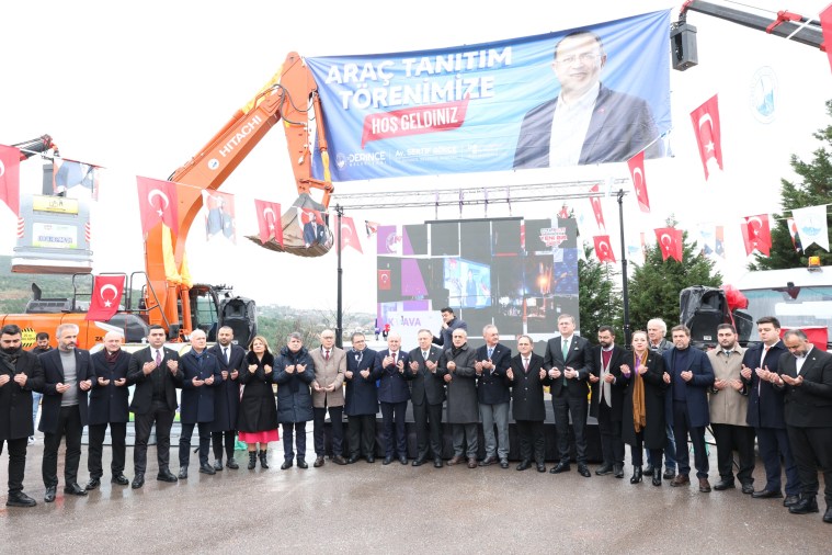 Açılış töreninde bir araya gelen kalabalık bir grup, araç tanıtım etkinliği için poz veriyor. Arka planda etkinlikle ilgili büyük bir afiş ve Türk bayrakları yer alıyor.