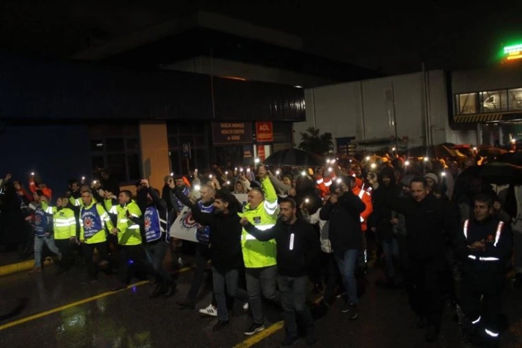 Gece saatlerinde düzenlenen protesto eyleminde, kalabalık bir grup yaya, telefon ışıklarıyla destek vererek yürüyüş yapıyor.