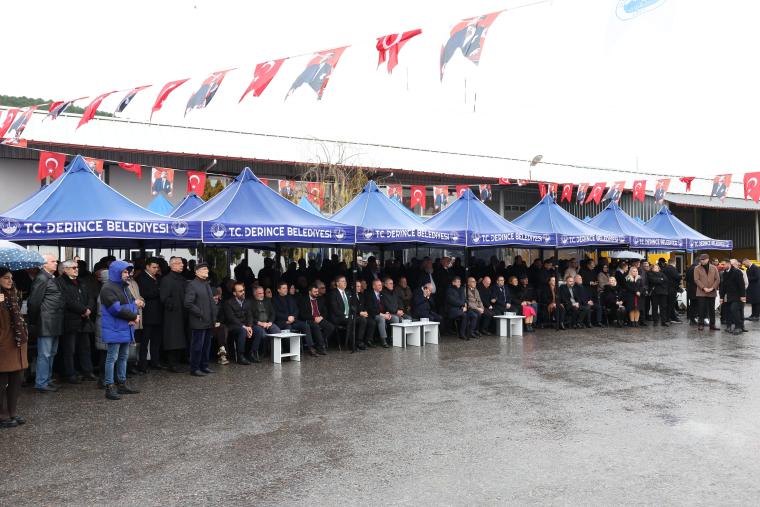 T.C. Derince Belediyesi önünde bir etkinlikte oturan kalabalık bir grup insan, şemsiyelerin altında duruyor. Arka planda Türk bayrakları asılı.