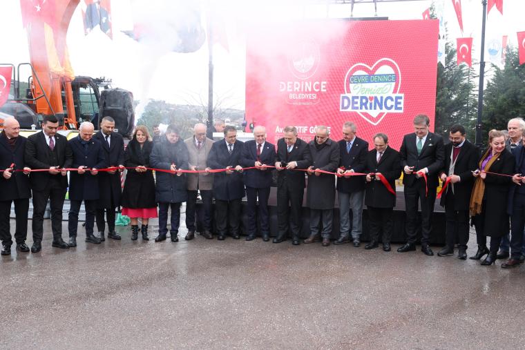 Derince Belediyesi açılış töreninde bir grup insan, büyük bir kırmızı kurdele kesiyor. Arka planda bir banner ve Türk bayrakları var.