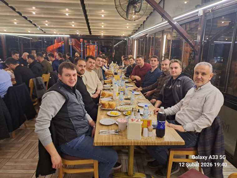 Bir restoranda oturan erkeklerden oluşan bir grup, uzun bir masanın etrafında, akşam yemeği sırasında gülümseyerek poz veriyor.