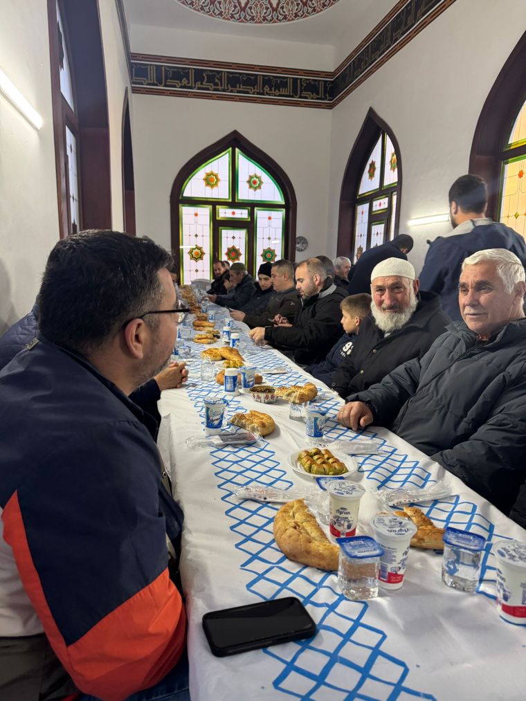 Bir grup insanın uzun bir masada oturarak yemek yediği, geleneksel Türk yiyeceklerinin sergilendiği bir görüntü.