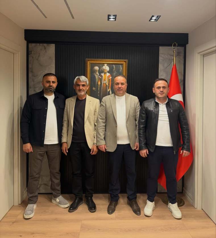 Dört erkek, bir Türkiye bayrağı ve bir tablo önünde poz veriyor.