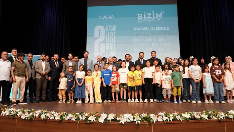 Bir etkinlikte poz veren yetişkinler ve çocuklar, arka planda 'Bizim' yazılı bir afiş ile.