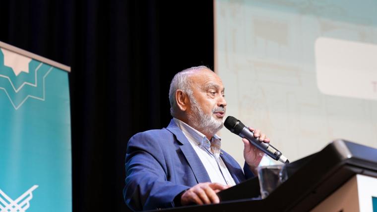 Bir konferansta mikrofonla konuşan yaşlı bir adam.